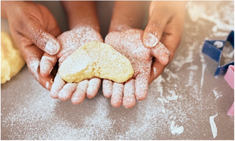 Child hands holding dough heart held by adult hands 