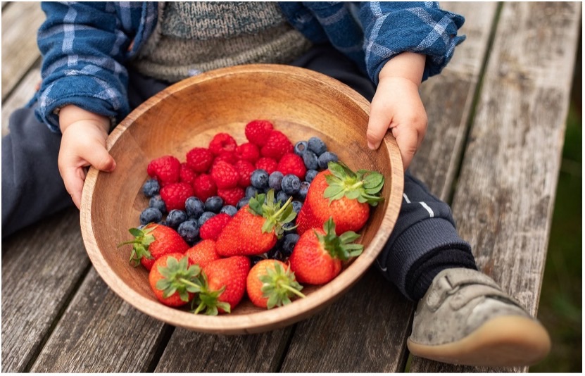 Child holding wooden bowl of fruit outside 