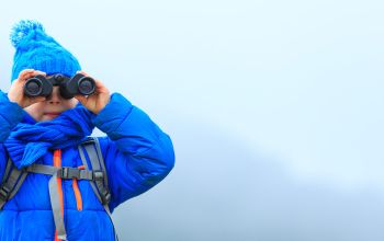 Young child with binoculars hiking in winter mountains.