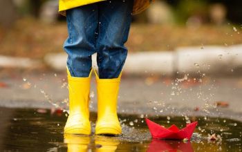 Yellow rainboots and origami boat in puddle