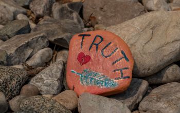 Roche peinte en orange sur laquelle on retrouve une plume bleue, un cœur brisé et le mot « vérité ».