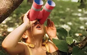 Child looking through homemade binoculars in a tree