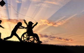 Happy child in wheelchair playing with children and kite at sunset.