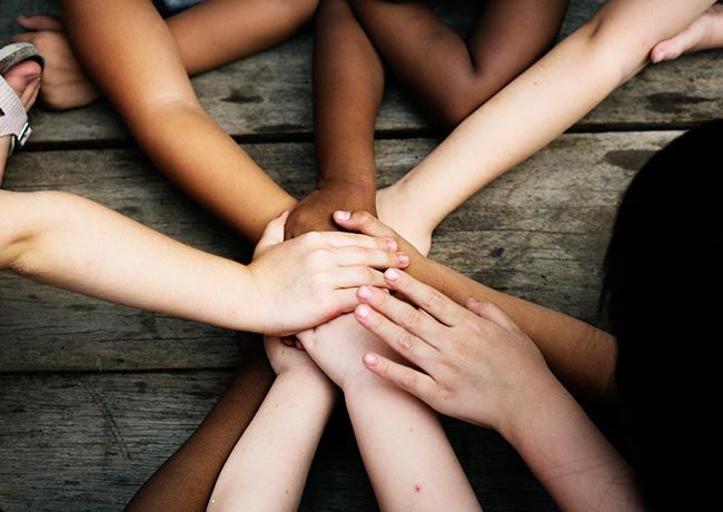 multiple children’s arms and hands with different skin tones placed one on top of the other.